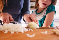 Madre enseñando a su hija a cortar cebollas - foto de stock