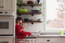 Девушка сидит на кухонном столе с лопаткой, поедающей глазурь — стоковое фото