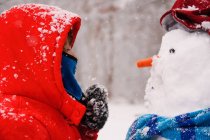 Chica de pie frente a un muñeco de nieve - foto de stock
