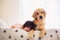 Girl lying on bed with golden retriever dog — Stock Photo