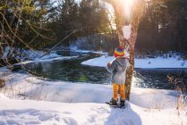 Menino em sapatos de neve em pé junto ao rio no inverno — Fotografia de Stock