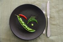 Pea pod with chili and dill over black plate — Stock Photo