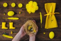 Yellow decorations and Girl hands holding nest with Easter eggs — Stock Photo