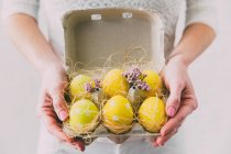 Mulher mãos segurando caixa com ovos de Páscoa pintados — Fotografia de Stock