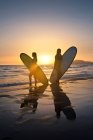 Due donne sulla spiaggia che trasportano tavole da surf al tramonto, Los Lances, Tarifa, Cadice, Andalusia, Spagna — Foto stock