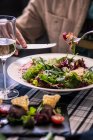 Женщина ест козий сыр и клубничный салат с бокалом белого вина — стоковое фото