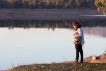 Menina em pé junto a um lago com seu ursinho de pelúcia — Fotografia de Stock