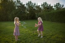 Dos chicas soplando burbujas en el jardín - foto de stock
