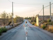 Rear view of woman walking down middle of the road, Majorca, Spain — Stock Photo