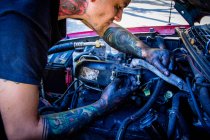 Человек с татуировками работает на автомобильном двигателе — стоковое фото