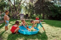 Quatro crianças brincando fora em uma piscina de remo no jardim — Fotografia de Stock