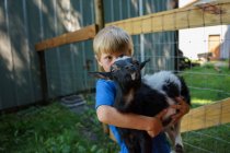 Boy carrying adorable goat on homestead — Stock Photo