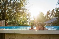 Menino olhando sobre a borda de uma piscina com irmãos no fundo — Fotografia de Stock