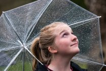 Fille debout sous la pluie avec un parapluie transparent — Photo de stock