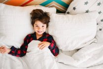 Portrait d'un garçon souriant couché au lit — Photo de stock