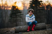 Junge sitzt lachend auf einem Baumstamm — Stockfoto