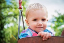 Портрет улыбающегося мальчика, сидящего на качелях — стоковое фото