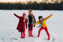 Tres niños de pie en la nieve con los brazos extendidos gritando - foto de stock