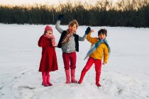 Tres niños de pie en la nieve con los brazos levantados gritando - foto de stock