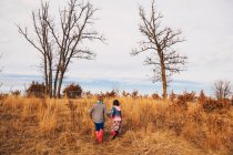 Boy and girl holding hands running in rural landscape — Stock Photo