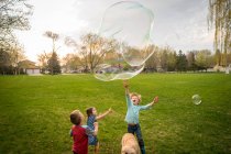 Três crianças brincando com bolhas de sabão gigantes — Fotografia de Stock