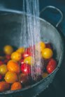 Cherry tomatoes in a colander under running water — Stock Photo