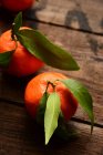 Clementinen mit Blättern auf einem Holztisch, Nahaufnahme — Stockfoto