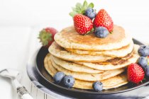 Stack of pancakes with maple syrup, fresh strawberries and blueberries — Stock Photo