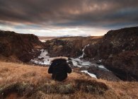 Visão traseira da mulher sentada em rochas olhando para o pôr do sol, Islândia — Fotografia de Stock