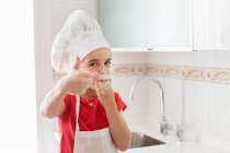 Retrato de un niño con un sombrero de chef lamiéndose los dedos - foto de stock