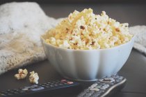 A bowl of popcorn with TV remote controls — Stock Photo