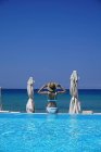 Frau im Bikini sitzt am Rande eines Swimmingpools am Meer — Stockfoto