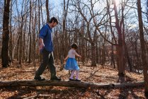 Padre e hija caminando sobre un tronco de árbol en el bosque - foto de stock