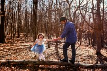 Padre e hija de pie sobre un tronco de árbol en el bosque - foto de stock
