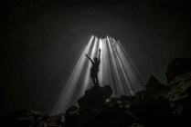 Silueta de un hombre de pie en una cueva con los brazos levantados, Jomblang, Java Central, Indonesia - foto de stock