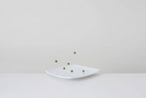Концептуальный зеленый горох, прыгающий на тарелке — стоковое фото