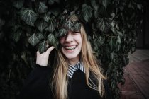 Mulher sorridente usando aparelho dentário escondido atrás de um arbusto hera — Fotografia de Stock