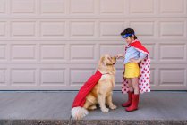Ragazza vestita da supereroe in piedi accanto al garage con il suo cane golden retriever — Foto stock