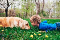 Menino e seu cão golden retriever deitado na grama olhando um para o outro — Fotografia de Stock