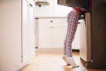 Chica de pie junto a un refrigerador abierto, vista lateral - foto de stock