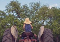 Vista trasera de una chica sentada en un tractor - foto de stock