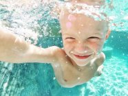 Sonriente niño nadando bajo el agua en una piscina - foto de stock