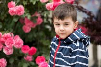 Retrato de un niño sonriente parado frente a un rosal - foto de stock