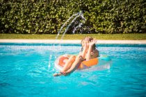 Junge sitzt auf einem aufblasbaren Gummiring im Schwimmbad und weicht einem Wasserstrahl aus — Stockfoto