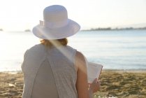 Femme assise à la plage lisant un livre — Photo de stock