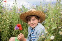 Lächelnder Junge, der in einem Feld von Wildblumen sitzt und einen Blumenstrauß hält — Stockfoto