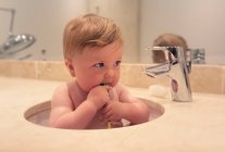 Baby boy sitting in a sink brushing his teeth — Stock Photo
