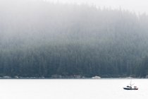 Small fishing boat off the wild, wooded Alaska coastline in the fog, near Juneau, Alaska, US — Stock Photo