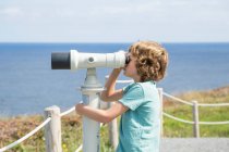 Menino em pé junto ao mar olhando através de um telescópio, Cantabria, Espanha — Fotografia de Stock