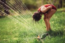 Girl playing in a sprinkler in the backyard — Stock Photo